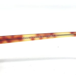 May include: Close-up of a portion of eyeglasses with a tortoiseshell pattern. The text "SPEC-SAVERS 183427" is printed on the arm of the glasses. The background is white.