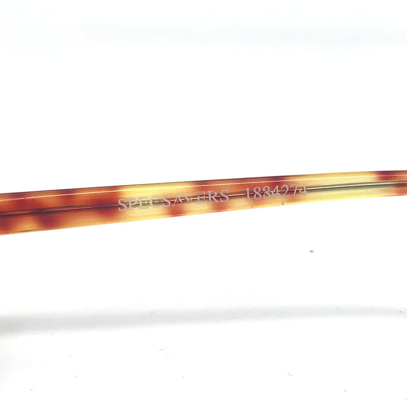 May include: Close-up of a portion of eyeglasses with a tortoiseshell pattern. The text "SPEC-SAVERS 183427" is printed on the arm of the glasses. The background is white.