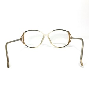 Puede incluir: Un par de gafas vintage con montura dorada y marr&oacute;n y lentes transparentes. La montura tiene una forma ovalada &uacute;nica con una ligera curva en la parte superior.