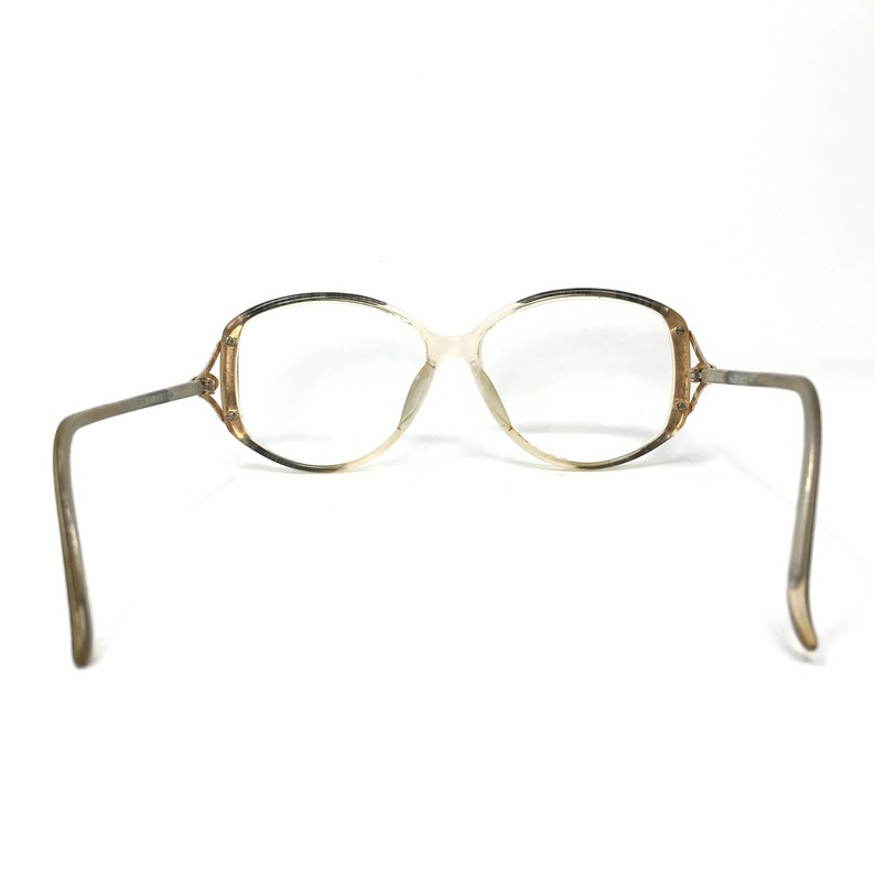 Puede incluir: Un par de gafas vintage con montura dorada y marr&oacute;n y lentes transparentes. La montura tiene una forma ovalada &uacute;nica con una ligera curva en la parte superior.