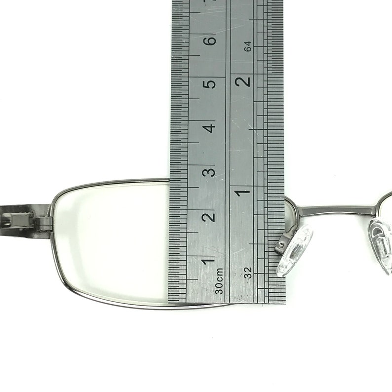 May include: Silver-framed eyeglasses with clear lenses are measured with a ruler. The ruler shows the glasses are approximately 3 inches wide. The glasses have nose pads and a hinge on the side.