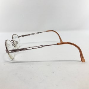 K&ouml;nnte beinhalten: Eine Brille mit silbernem Gestell und braunen B&uuml;geln. Das Gestell hat ein einzigartiges, wellenf&ouml;rmiges Design.