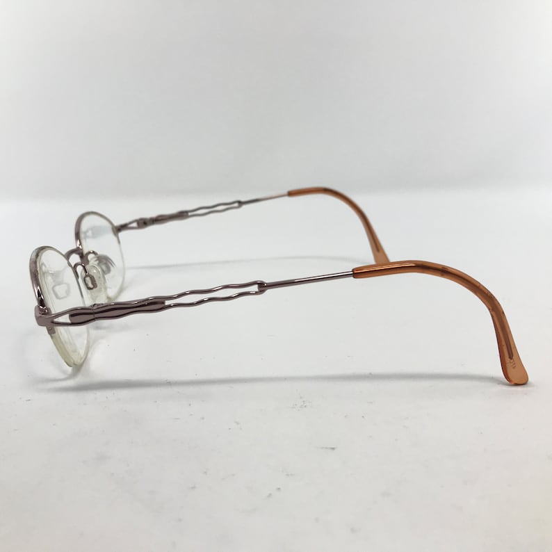 K&ouml;nnte beinhalten: Eine Brille mit silbernem Gestell und braunen B&uuml;geln. Das Gestell hat ein einzigartiges, wellenf&ouml;rmiges Design.