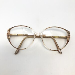 May include: Clear eyeglasses with a brown and gold patterned frame. The frame has a rounded oval shape.
