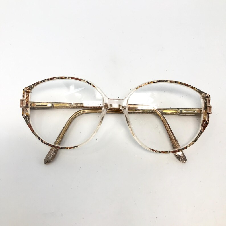 May include: Clear eyeglasses with a brown and gold patterned frame. The frame has a rounded oval shape.
