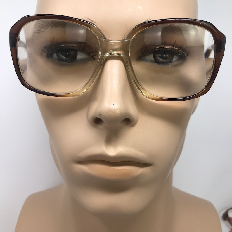 May include: Vintage eyeglasses with a brown and tan gradient frame. The square-shaped lenses are clear. The glasses are displayed on a mannequin head.