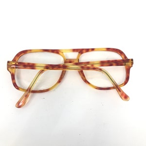 May include: Vintage eyeglasses with a tortoiseshell pattern. The frames have a rectangular shape with a double bridge and thick temples. The lenses are clear, and the glasses are set against a white background.