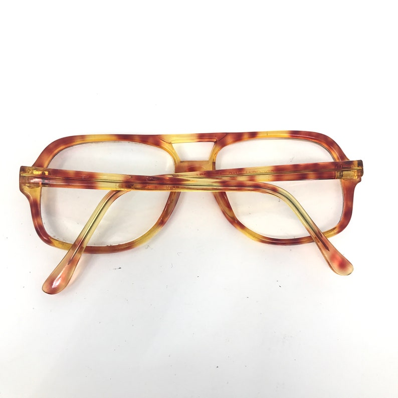 May include: Vintage eyeglasses with a tortoiseshell pattern. The frames have a rectangular shape with a double bridge and thick temples. The lenses are clear, and the glasses are set against a white background.