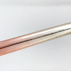 May include: Close-up of a clear, pink-tinted plastic arm of a pair of glasses. The arm is inscribed with the text "SPECSAVERS 590139".