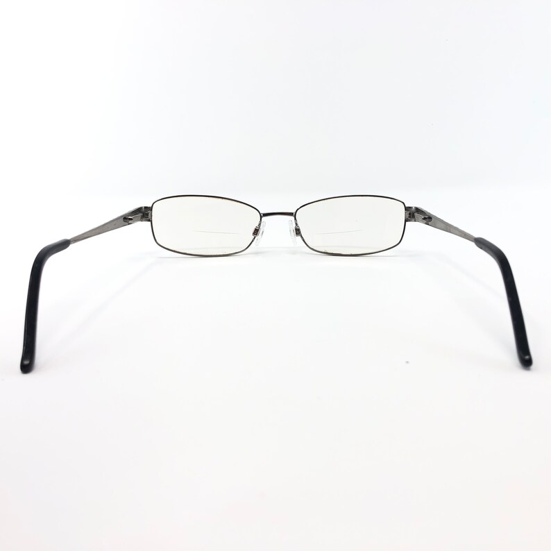 May include: Rectangular eyeglasses with a dark metal frame and black temples. The lenses have a bifocal design. The glasses are set against a white background.