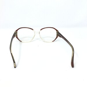 May include: Vintage eyeglasses with a clear frame and brown accents. The glasses have a rounded shape and brown arms. The lenses are clear. The glasses are set against a white background.