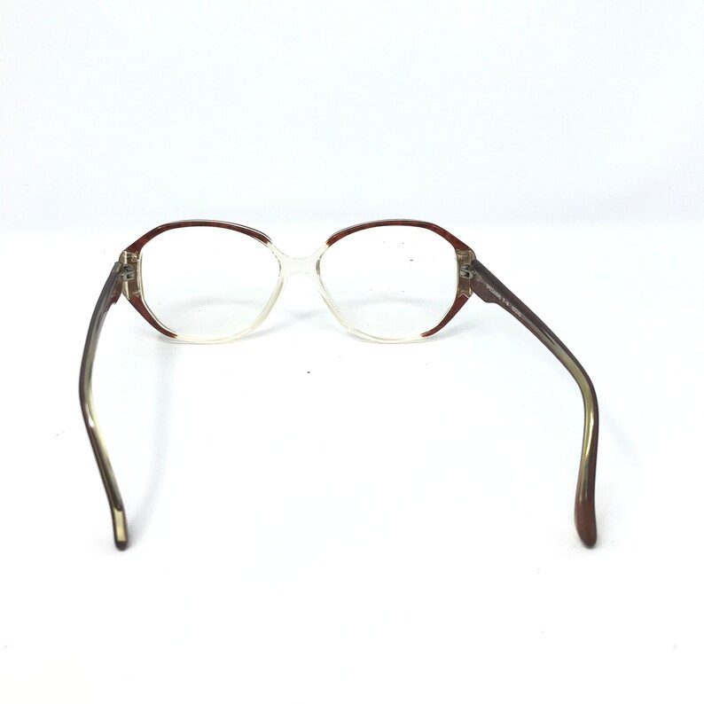 May include: Vintage eyeglasses with a clear frame and brown accents. The glasses have a rounded shape and brown arms. The lenses are clear. The glasses are set against a white background.