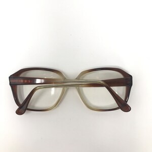 May include: Brown and tan eyeglasses with a rectangular frame. The glasses have a gradient effect, transitioning from a darker brown at the top to a lighter tan towards the bottom. The temples are a solid brown color.