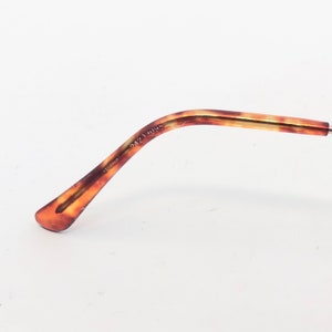 May include: A close-up of the arm of a pair of eyeglasses. The arm features a tortoiseshell pattern in shades of brown and amber. The text "2423 095" is printed on the arm. The background is white.