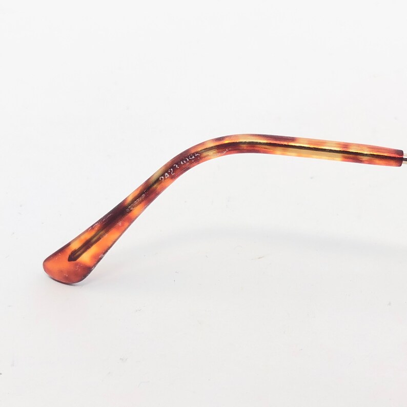 May include: A close-up of the arm of a pair of eyeglasses. The arm features a tortoiseshell pattern in shades of brown and amber. The text "2423 095" is printed on the arm. The background is white.