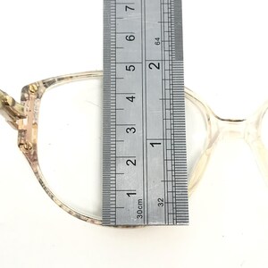 May include: Close-up of a pair of eyeglasses with a tortoiseshell frame and clear lenses. The frame is measured with a ruler, showing a width of 1 1/2 inches.