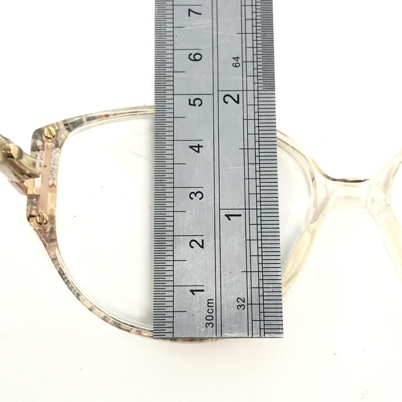 May include: Close-up of a pair of eyeglasses with a tortoiseshell frame and clear lenses. The frame is measured with a ruler, showing a width of 1 1/2 inches.