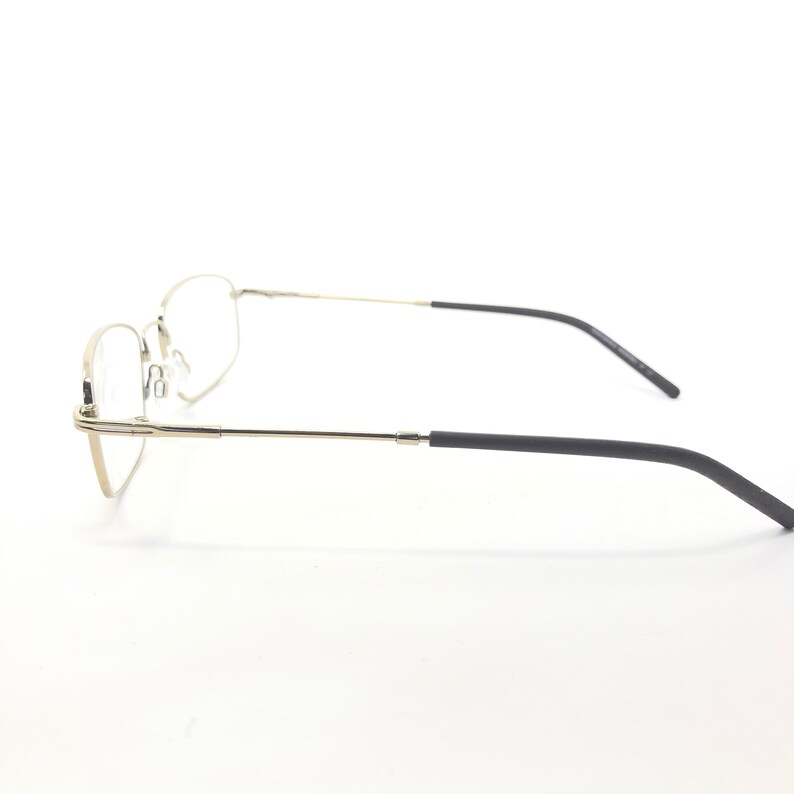 May include: A pair of eyeglasses with a silver metal frame and black temples. The lenses are clear, and the glasses are set against a white background. The design is minimalist and modern.