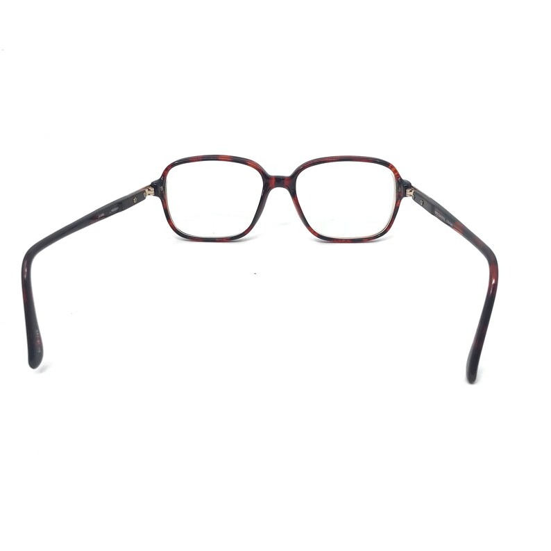May include: Eyeglasses with a tortoiseshell pattern frame and rectangular lenses. The temples are dark brown and extend outward. The glasses are set against a white background.