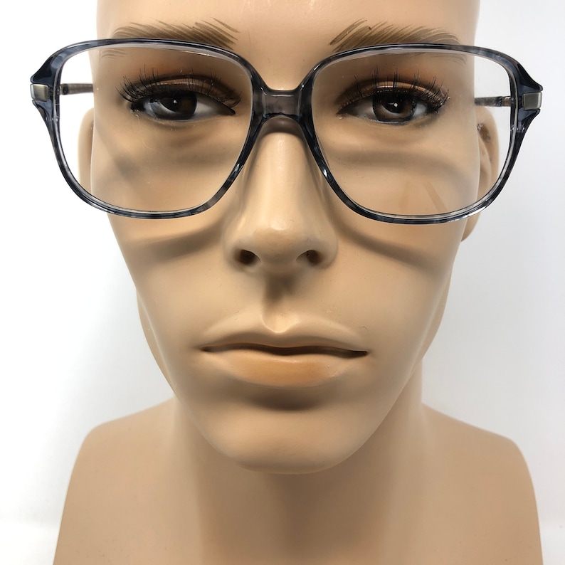 May include: Square-framed spectacles with a translucent grey and black speckled design. The spectacles have a thick frame and a metal bridge. The lenses are clear. The spectacles are displayed on a mannequin head.
