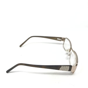 May include: A pair of eyeglasses with a rectangular frame. The glasses have a brown and silver color scheme. The temples are brown, and the frame around the lenses is silver. The temple arms are thin and curve down to the ear.