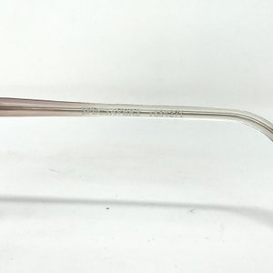 May include: Close-up of the arm of a pair of eyeglasses. The frame is a light, translucent color with the text "SPECSAVERS 1034275" printed on the arm. The background is white.