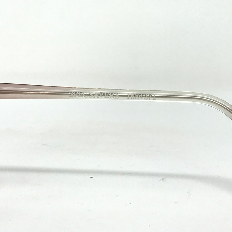 May include: Close-up of the arm of a pair of eyeglasses. The frame is a light, translucent color with the text "SPECSAVERS 1034275" printed on the arm. The background is white.