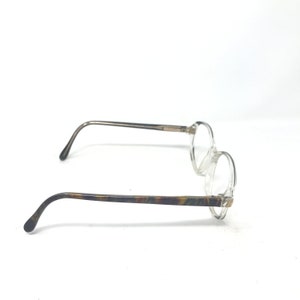 May include: Clear, round-framed spectacles with a thin, silver-toned metal bridge and arms. The earpieces feature a tortoiseshell pattern. The glasses are set against a white background.