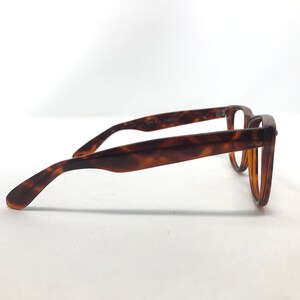 May include: A pair of eyeglasses with a classic tortoiseshell pattern. The frames are a warm brown with darker brown accents. The glasses have a rectangular shape and are viewed from the side, showcasing the arm and the lens.