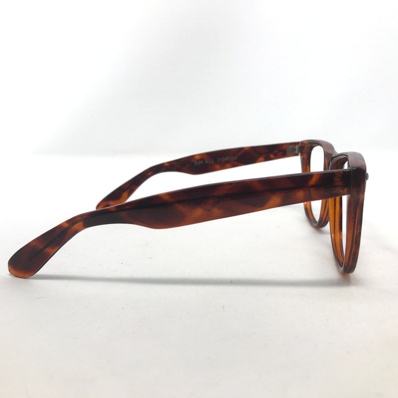 May include: A pair of eyeglasses with a classic tortoiseshell pattern. The frames are a warm brown with darker brown accents. The glasses have a rectangular shape and are viewed from the side, showcasing the arm and the lens.