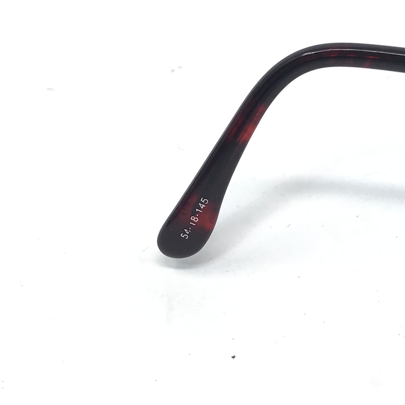 May include: Close-up of the temple arm of eyeglasses. The arm is a dark brown with a tortoiseshell pattern. The size is printed on the arm: 54-18-145.