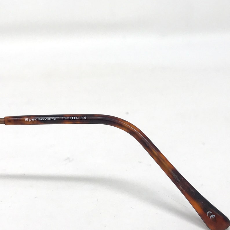 May include: Close-up of a brown and tan tortoiseshell eyeglasses arm. The text "Specsavers 1938434" is printed on the arm. The arm is curved and has a rounded tip.