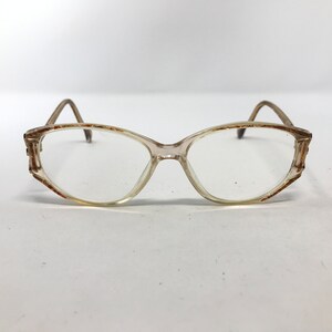 May include: Clear-framed eyeglasses with a light brown tint. The frames have a rectangular shape with rounded edges. The temples and the edges of the frames have a brown and orange pattern. The glasses are set against a white background.