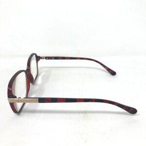 May include: A pair of eyeglasses with a tortoiseshell pattern on the frames and temples. The frames are a reddish-brown color, and the temples have a black and red striped design. The glasses have a gold-colored metal accent at the hinges.