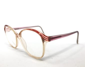 Könnte beinhalten: Vintage-Brille mit rosafarbenem und rotem Gestell. Das Gestell hat eine abgerundete Form und klare Gläser.