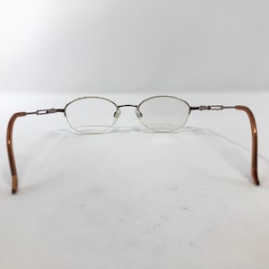 K&ouml;nnte beinhalten: Eine Brille aus braunem Metall mit ovalen Gl&auml;sern. Die B&uuml;gel der Brille sind braun und haben ein dekoratives Design.