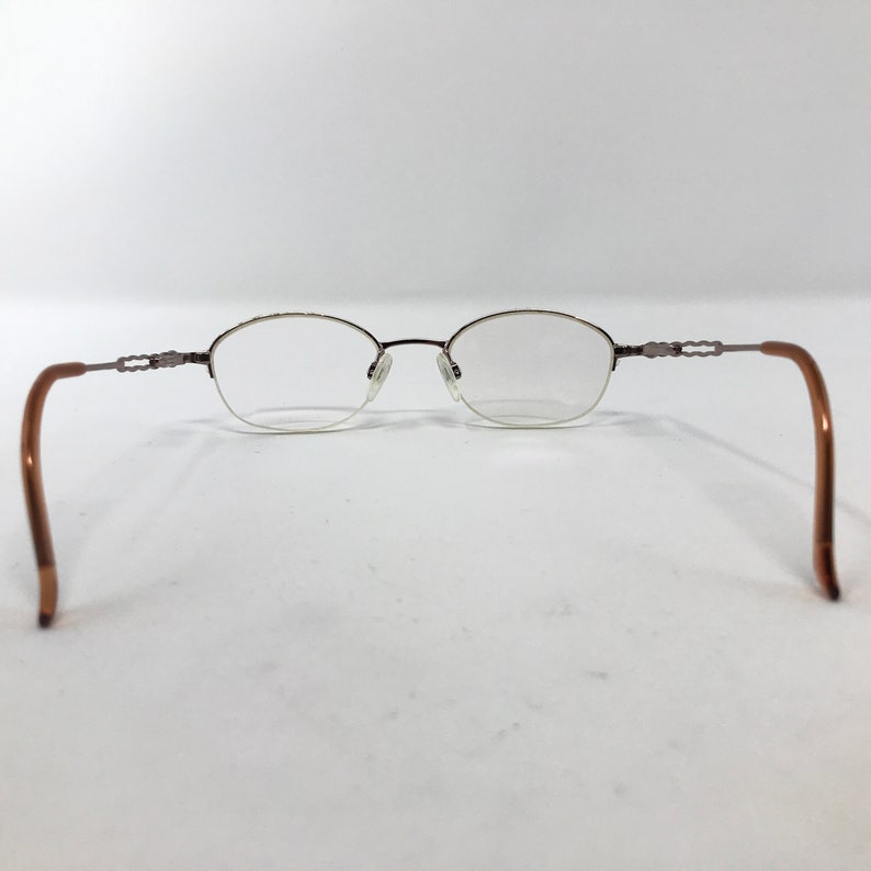 K&ouml;nnte beinhalten: Eine Brille aus braunem Metall mit ovalen Gl&auml;sern. Die B&uuml;gel der Brille sind braun und haben ein dekoratives Design.