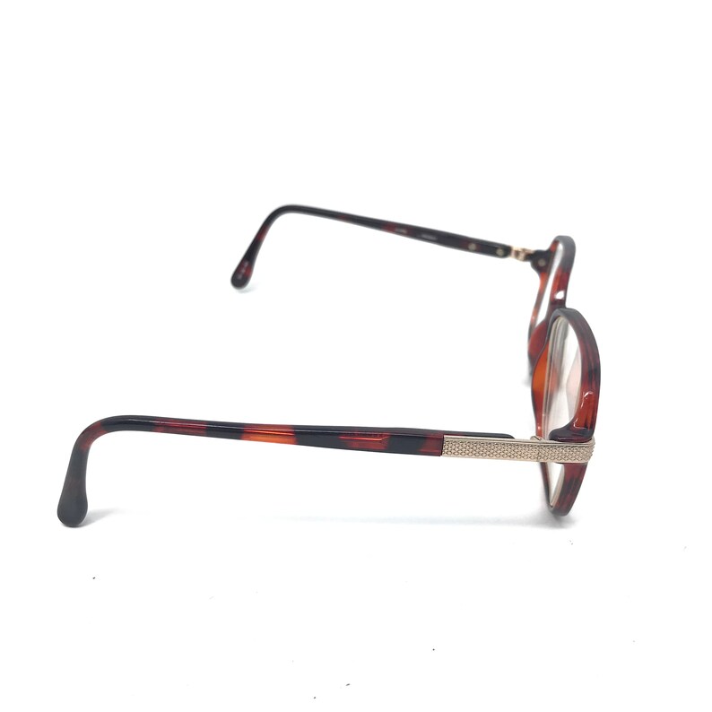 May include: A pair of eyeglasses with a tortoiseshell pattern on the frames. The glasses have a round shape and feature a silver-colored accent on the temples. The lenses are clear.