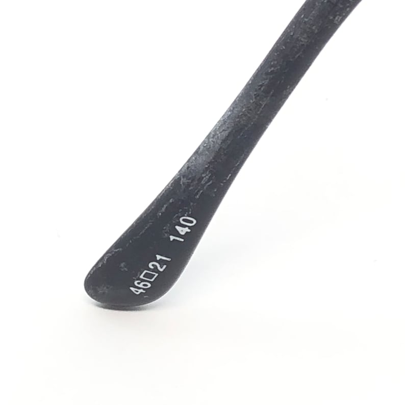 May include: Close-up of a black eyeglass arm with the measurements 46▢21 140 printed in white. The arm is textured and tapers to a rounded end.
