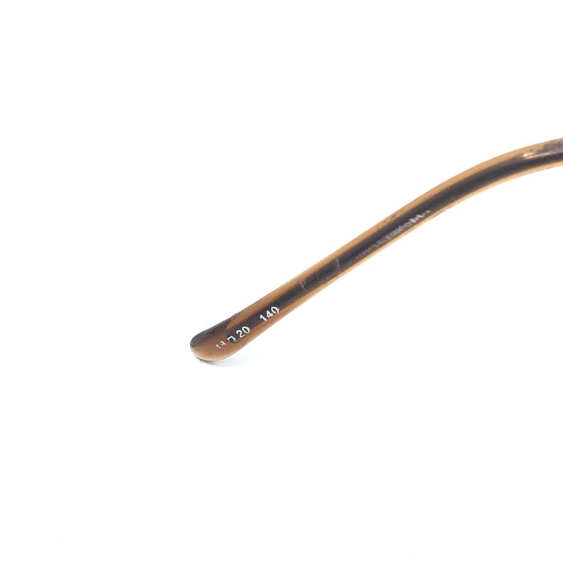 Puede incluir: Primer plano de una patilla de gafas marr&oacute;n. La patilla tiene un color degradado y los n&uacute;meros 13 20 140 est&aacute;n impresos en la patilla. El fondo es blanco.