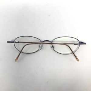 May include: Oval-shaped eyeglasses with a thin, dark blue frame and gold-colored temples. The glasses have clear lenses and nose pads. The design is minimalist and modern, suitable for everyday wear.