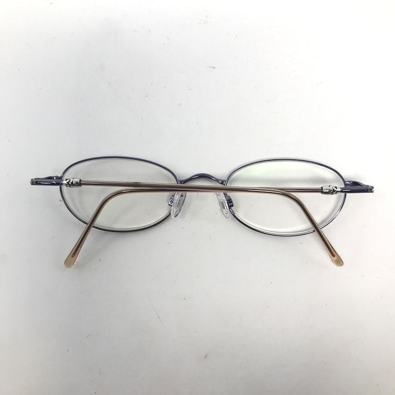 May include: Oval-shaped eyeglasses with a thin, dark blue frame and gold-colored temples. The glasses have clear lenses and nose pads. The design is minimalist and modern, suitable for everyday wear.