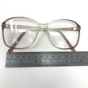 May include: Clear eyeglasses with a light brown gradient frame. The glasses have a rectangular shape and are placed on a white surface next to a ruler. The frame measures approximately 5 inches in width.