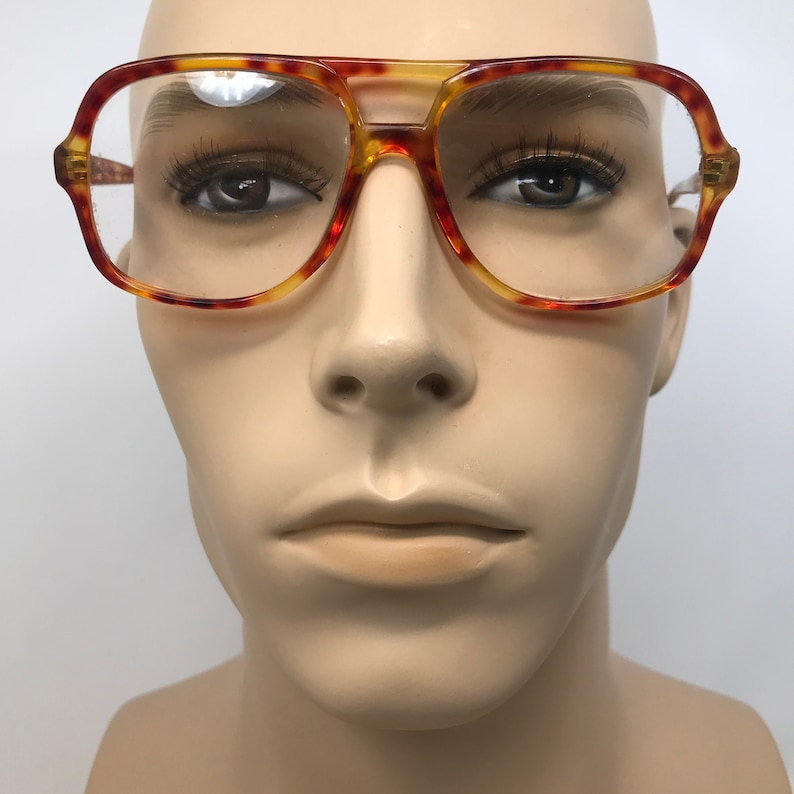 May include: Vintage eyeglasses with a tortoiseshell pattern. The frames are a combination of amber, red, and yellow hues. The lenses are clear, and the glasses have a classic aviator shape.