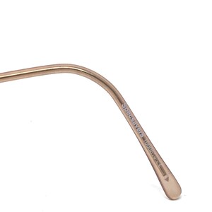 May include: Close-up of a gold-coloured eyeglass frame arm. The text "Specsavers 10008" is printed on the arm. The frame has a curved design and a rounded tip.