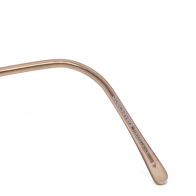 May include: Close-up of a gold-coloured eyeglass frame arm. The text "Specsavers 10008" is printed on the arm. The frame has a curved design and a rounded tip.