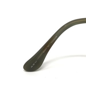 K&ouml;nnte beinhalten: Nahaufnahme des B&uuml;gels einer olivgr&uuml;nen Unisex-Brille. Auf dem Brillenb&uuml;gel steht der Text "UNISEX 163" und "24249409". Am Ende des B&uuml;gels stehen die Zahlen "49 20 133".