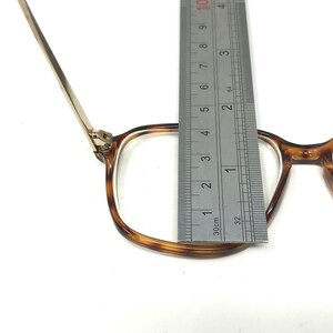 K&ouml;nnte beinhalten: Eine Brille mit Schildpattgestell und goldenen Metallb&uuml;geln. Die Brille wird mit einem Lineal gemessen, wobei die Breite des Gestells 3,5 cm betr&auml;gt.