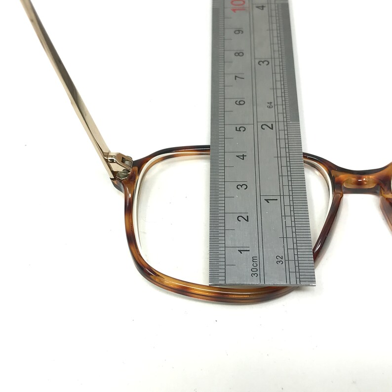 K&ouml;nnte beinhalten: Eine Brille mit Schildpattgestell und goldenen Metallb&uuml;geln. Die Brille wird mit einem Lineal gemessen, wobei die Breite des Gestells 3,5 cm betr&auml;gt.