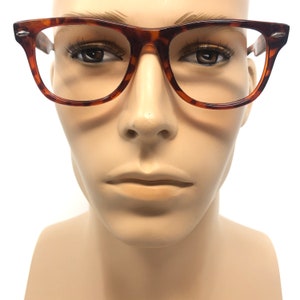 K&ouml;nnte beinhalten: Eine Brille mit Schildpattmuster und rechteckigem Rahmen. Die Brille hat ein braunes und bernsteinfarbenes Muster und wird auf einem Schaufensterkopf pr&auml;sentiert. Die Fassungen haben einen kleinen silbernen Akzent an den B&uuml;geln.